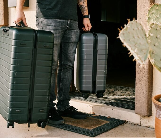 man in black denim jeans and black leather shoes standing beside black luggage bag