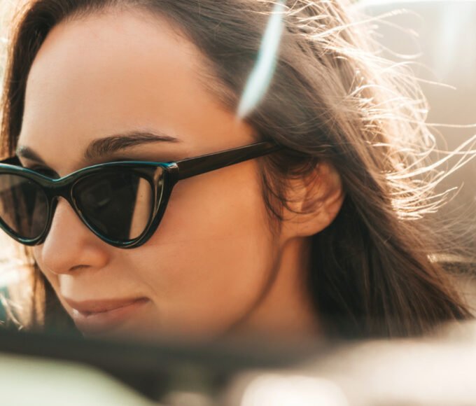 A woman with polarized sunglasses on in the rear view mirror.
