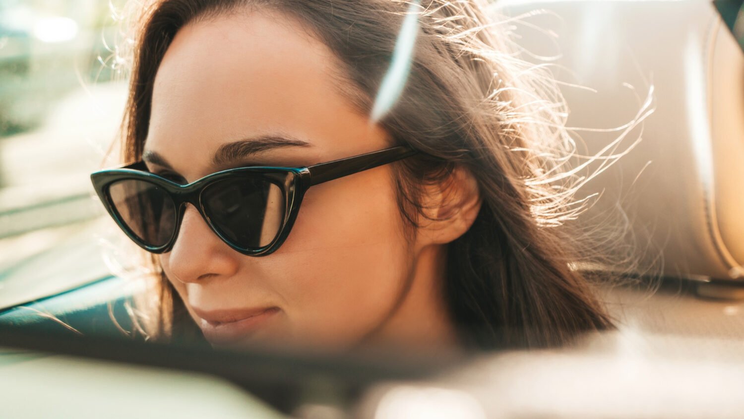 A woman with polarized sunglasses on in the rear view mirror.